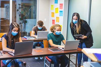 High school students and teacher wearing face masks and social distancing in classroom setting