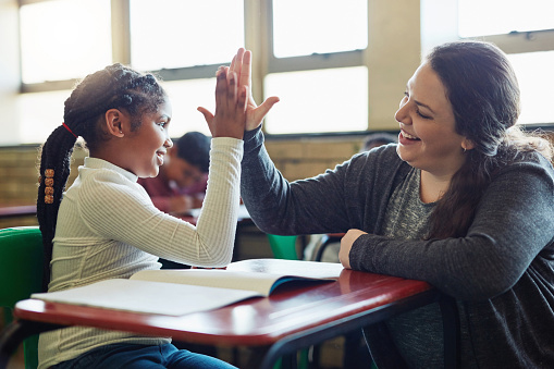 young girl giving her teacher a high five in the classroom