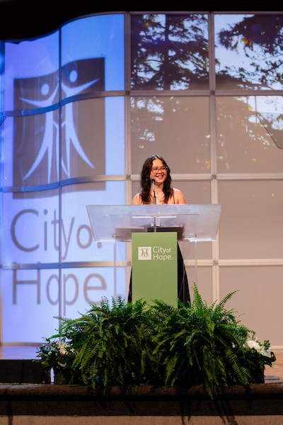 IHFI patient speaker Caitlin Herron standing on stage behind a podium