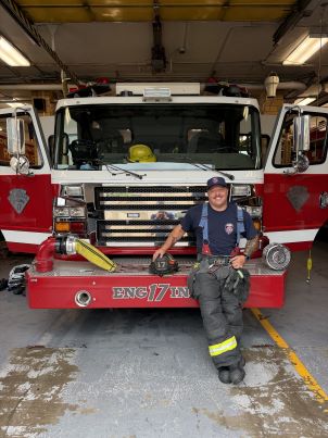 Cody Duge in uniform standing in front of fire engine