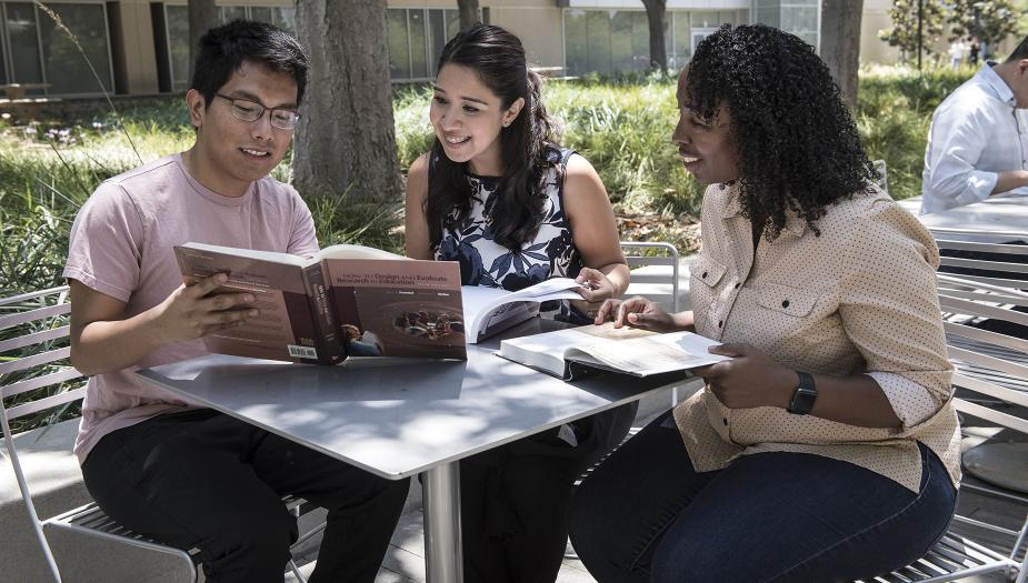 Three graduate students looking at a text book
