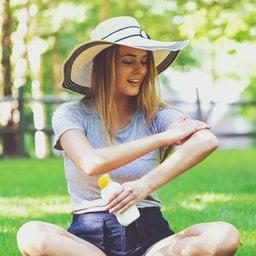 Women wearing wide brim hat applies sunscreen to reduce exposure to UV light.