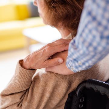 A midsection of man standing behind woman in wheelchair indoors at home