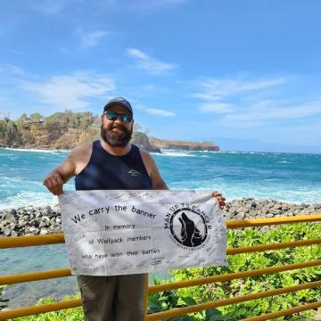 City of Hope colon cancer patient Jason Randall holds a Man Up to Cancer banner with the ocean behind him