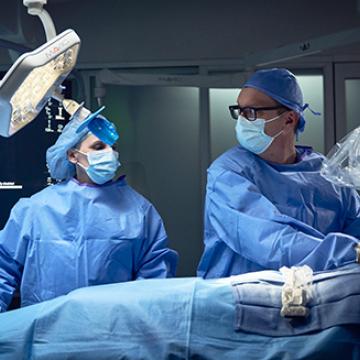 Two surgeons in sterile scrubs and masks performing a surgical procedure in an operating room.