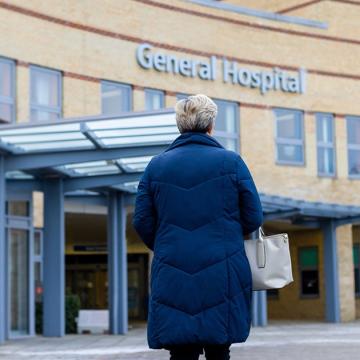 image of a woman in a coat looking at the front entrance of a general hospital