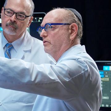 image of two doctors wearing lab coats and yamecas while looking at something on a wall