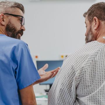 image from behind of a doctor in scrubs talking to a patient in a hospital gown