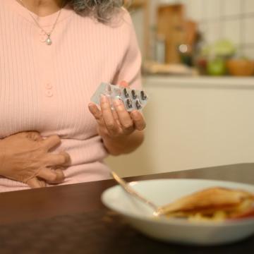 woman sitting at table holding medication and clutching stomach