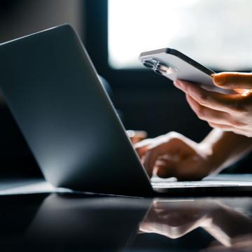 Person working on a laptop and looking at their phone