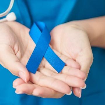 Female practitioner cupping hands and holding a blue cancer ribbon