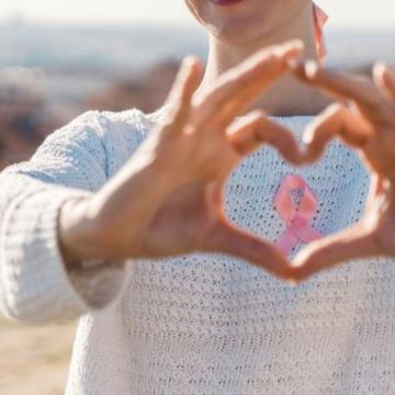 woman making a heart symbol with hands in front of pink ribbon on sweater