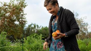 A woman walking through a garden holding vegetables