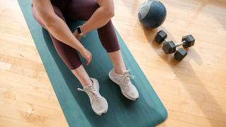 Woman sitting on exercise mat next to dumbbells  