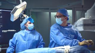 Two surgeons in sterile scrubs and masks performing a surgical procedure in an operating room.
