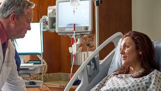 doctor speaking with a woman in a hospital bed and a man sitting beside her