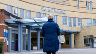image of a woman in a coat looking at the front entrance of a general hospital