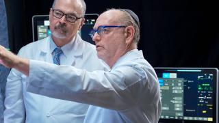 image of two doctors wearing lab coats and yamecas while looking at something on a wall
