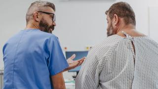 image from behind of a doctor in scrubs talking to a patient in a hospital gown
