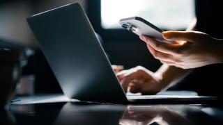 Person working on a laptop and looking at their phone