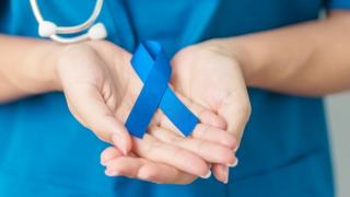 Female practitioner cupping hands and holding a blue cancer ribbon