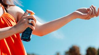 Woman spraying her arm with sunscreen