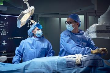 Two surgeons in sterile scrubs and masks performing a surgical procedure in an operating room.