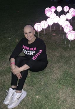 Imelda Jordan sitting in front of a cancer awareness symbol made of lit lanterns